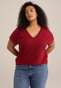 Maglietta rossa a V con un motivo a foglia testurizzato, maniche corte e vestibilità comoda, abbinata a jeans azzurri chiari.