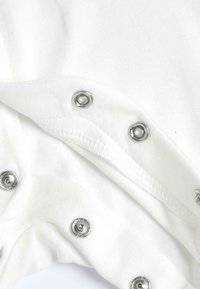 Tessuto bianco con chiusure a scatto metalliche lungo il bordo, che mostra una texture liscia e un design piegato, evidenziando gli accenti argentati.