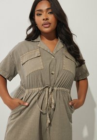 Olivgrön skjortklänning med korta ärmar, två bröstfickor, knappstängning och dragsko i midjan. Slätt, lätt tyg.