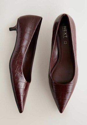 Viininpunaiset kärjestä terävät kengät, joissa on krokotiilinsolki kuvioitu nahkapinta, matala korko ja avoimet sivut. Sisäpuolella näkyy tuotemerkin nimi "NEXT."