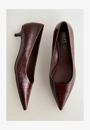Bordowe buty z noskiem w szpic, wykonane z tłoczonej skóry imitującej krokodyla, z niskim obcasem i odkrytymi bokami. Wnętrze z nazwą marki "NEXT".