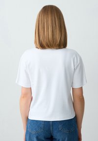 Witte T-shirt met korte mouwen en een rechte zoom, gecombineerd met hoge blauwe denim jeans. Glad materiaal, casual pasvorm.