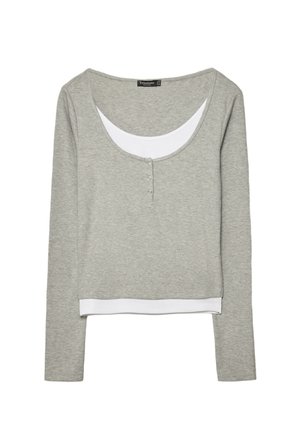 Hellgraues Langarm-Oberteil mit Lagenoptik, weißem inneren Ausschnitt und Saumdetaillen, mit einem Rundhalsausschnitt und drei kleinen Knöpfen auf der Vorderseite.