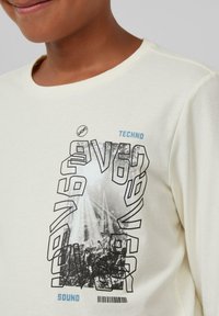 Cremfarbener Longsleeve-T-Shirt mit einem grafischen Druck, der den Text "TECHNO" und "SOUND" sowie eine Konzertszene in Schwarz-Weiß zeigt.