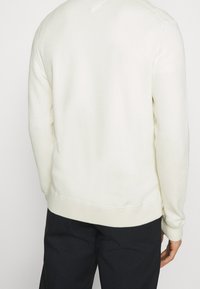 Cremfarbener Sweatshirt mit strukturiertem Strick, gerippten Bündchen und Saum. Verfügt über einen V-förmigen Ausschnitt und ein sauberes, minimalistischem Design.