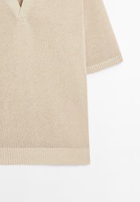 Beige pletený pulovr s výstřihem ve tvaru V a krátkými rukávy. Má žebrované manžety a spodní lem, což podtrhuje hladkou strukturu a jednoduchý design.