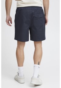 Donkertblauwe shorts met een losse pasvorm, elastische tailleband en een achterzak met knoop. Het materiaal lijkt lichtgewicht met een gladde textuur.