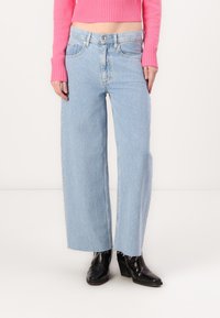 Light blue wide-leg jeans with raw hems, five pockets, and a button fly, made of denim fabric, paired with black heeled boots.