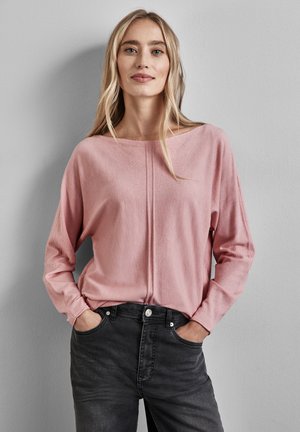Maglione lungo a maniche lunghe di colore rosa, con una vestibilità ampia, scollo largo e un dettaglio cucito centrale, abbinato a jeans grigi scuri. Texture morbida.