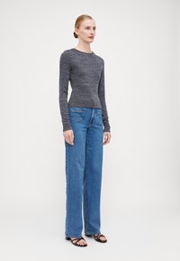 Haut en maille grise ajusté à manches longues, associé à un jean bleu à jambes larges avec poches arrière. Le mannequin porte des sandales à talons noires.