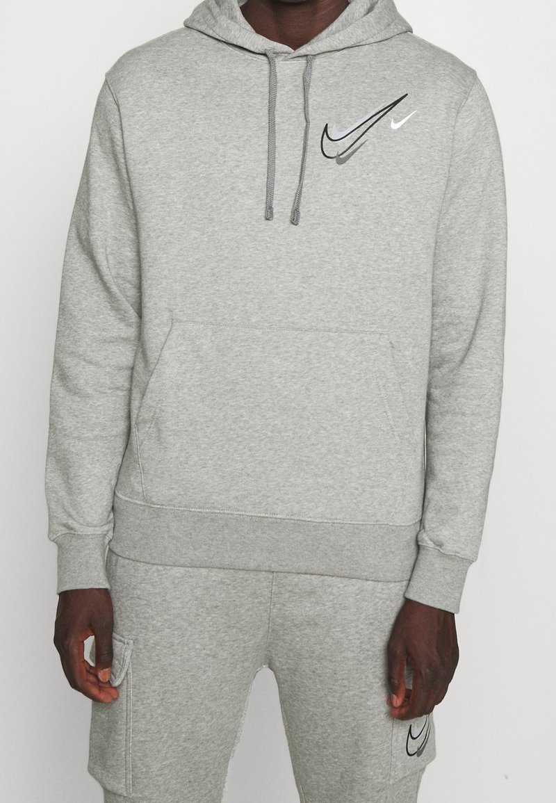 Sudadera gris hecha de tela suave, con un bolsillo frontal, capucha con cordón y dos logotipos de Nike en blanco y negro en el pecho.