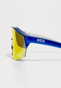 Blaue Sportsonnenbrille mit gelben Verlaufsgläsern, einem eleganten Design und silbernen Akzenten. Verfügt über ein markantes Logo auf dem Gestell.