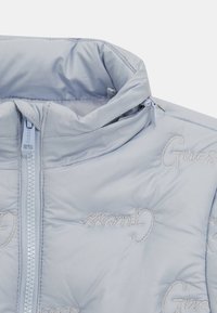 Jasnoniebieska pikowana kurtka z haftowanymi logo "Guess", z wysokim kołnierzem i przednim zamkiem błyskawicznym. Gładki materiał z delikatnym połyskiem.