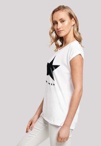 White cotton t-shirt with a large black star graphic and smaller star accents. Short sleeves and a relaxed fit.