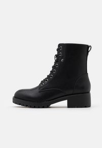 Botas de cuero negro hasta el tobillo con punta redonda, cordones en la parte delantera y una suela de goma texturizada. Presenta ojetes de metal y un pequeño tacón.