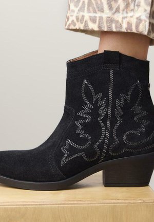 Stivale alla caviglia in suede nero con intricate cuciture bianche sui lati, punta quadrata e tacco basso a blocco. Finitura texturizzata.