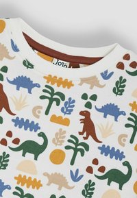 T-shirt en coton avec un col rond, présentant un motif coloré de dinosaures et de plantes en vert, bleu, marron et orange sur fond blanc.