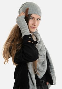 Grijze gebreide beanie met een bruine leren logo patch, bijpassende vingerloze handschoenen en een oversized gestructureerde sjaal, allemaal gemaakt van zachte materialen.