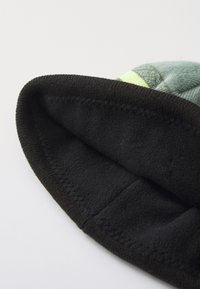 Chapeau noir doublé en polaire avec un extérieur à motif vert et un bord noir contrastant. Texture douce, design plié.