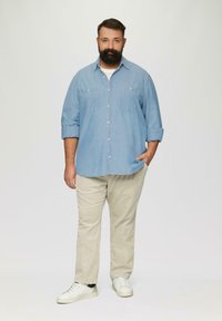 Lichtblauwe overhemd met knopen, voorzien van twee borstzakken, beige broek en witte sneakers. Het overhemd heeft opgerolde mouwen en een relaxed fit.