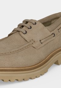 Μπεζ δερμάτινο παπούτσι με κορδόνια, ραμμένες λεπτομέρειες, μεταλλικά οπές κορδονιών, μαξιλαρωμένο κολάρο και παχύ σόλα από καουτσούκ με έντονο ανάγλυφο.