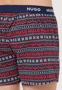 Șorturi de baie cu model, de culoare albastru marin, cu inscripționarea roșie "HUGO", fulgi de zăpadă și desene cu reni. Talie elastică, material din poliester.