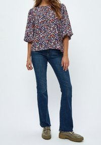 Blusa con motivo floreale e maniche larghe nei toni del blu, arancione e rosa, abbinata a jeans a zampa scuri e scarpe platform verde oliva.