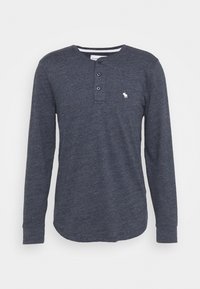 Tmavě modrá dlouhá mužská košile typu henley z texturované bavlny, se zapínáním na tři knoflíky a malým bílým logem. Zaoblený spodek.