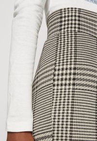 Tela a cuadros en blanco y negro con un patrón de espiga, combinada con una blusa de manga larga blanca. Muestra una textura suave y un diseño ajustado.