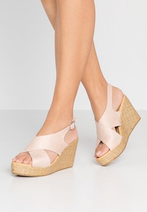 Sandalias de cuña con diseño de tiras cruzadas, material suave de ante beige, punteras abiertas y plataforma con textura natural tejida. Correa ajustable en el tobillo.
