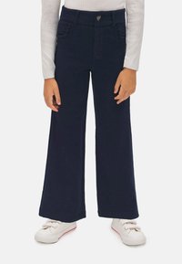 Pantalones de pierna ancha en azul marino, fabricados en algodón, que cuentan con dos bolsillos frontales, una cinturilla de altura media y un pequeño emblema decorativo en la cintura.