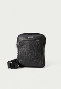 Črno Guess torbico čez ramo z vtisnjenimi vzorci logotipa, sprednjim žepom na zadrgo in nastavljivim trakom na enobarvni podlagi.