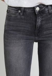 Jeans ajustados de talle alto en negro con una textura desgastada, diseño de cinco bolsillos y cierre de botón de metal, que destacan detalles de costura.