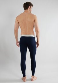 Leggings de color azul marino con una textura suave y cinturilla elástica plateada, estilo ajustado, costuras visibles y sin patrones. Modelo visto desde la parte de atrás.