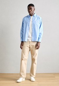 Lichtblauw, knoopsluiting shirt met een geruit patroon, gedragen over een wit t-shirt, gecombineerd met beige broek en witte sneakers.