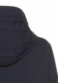 Veste à capuche bleue marine avec une texture lisse et des détails de coutures visibles. Dotée d'une capuche arrondie et d'un design sans couture au niveau du cou.