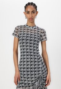 Sheer dress in black and white geometric pattern, featuring short sleeves, a high neckline, and side ruching detail.