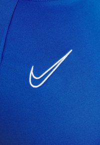 Blue athletic shirt featuring a textured fabric and a prominent white Nike swoosh logo. The design is smooth and fitted.
