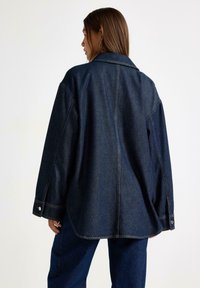 Denimjacka i mörkblått med avslappnad passform, spetsig krage, stor ryggsöm och knäppte manchetter med silverdetaljer.