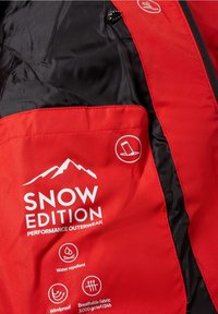 Tissu d'extérieur rouge et noir étiqueté « SNOW EDITION PERFORMANCE OUTERWEAR » avec des icônes indiquant des caractéristiques déperlantes, coupe-vent et respirantes.