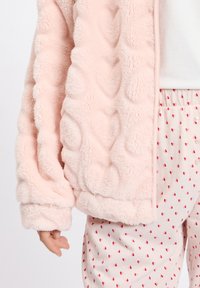 Jasnoróżowa, puszysta kurtka z teksturowanej tkaniny, z zaokrąglonymi wzorami, w połączeniu z kremowymi spodniami ozdobionymi czerwonymi nadrukami serc.