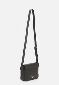 Černá crossbody taška z umělé kůže s plochým obdélníkovým tvarem, nastavitelným popruhem, magnetickým klopovým zapínáním a zlatým logem na přední straně.