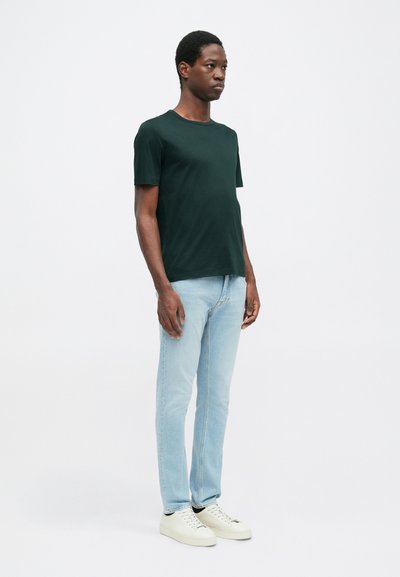 Πράσινο κοντομάνικο μπλουζάκι από βαμβάκι, σε συνδυασμό με ανοιχτό μπλε τζιν και λευκά αθλητικά. Η εφαρμογή είναι χαλαρή, με στρογγυλή λαιμόκοψη.