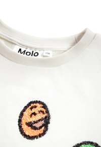 Vit bomull t-shirt med tre färgglada, paljettprydda leende ansikten i orange, svart och grön. Rund halsringning och mjuk textur.