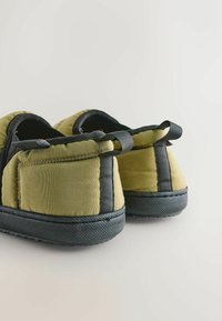 Zelené prešívané papuče s čiernymi gumovými podrážkami, so malými látkovými slučkami vzadu pre jednoduché obutie. Textúrovaný vrchný materiál.