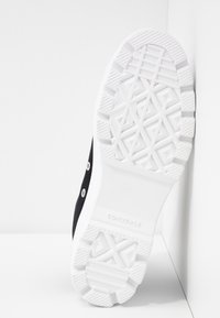 Černé plátěné tenisky s bílou gumovou podrážkou. Obsahují texturovaný vzorek na podrážce a kovové očka na tkaničky. Branding Converse na podrážce.