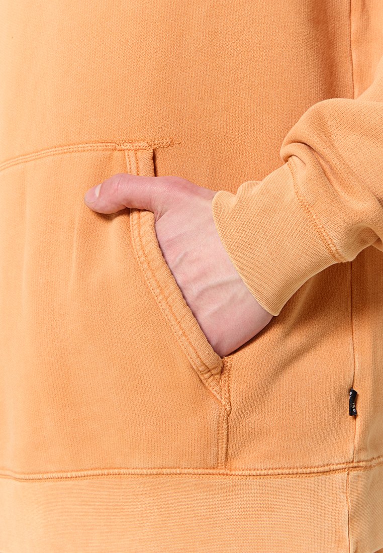 Orange Kapuzenpullover mit Kängurutasche, gerippten Bündchen und gesteppten Details. Der Stoff wirkt weich mit einer strukturierten Oberfläche.