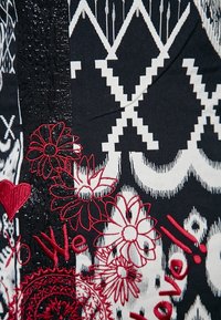 Tessuto bianco e nero con motivi geometrici e ricami floreali rossi. Texture aggiuntive includono un accento in pizzo nero.