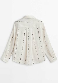 Camicia bianca a maniche lunghe con colletto, caratterizzata da strisce verticali nere e dettagli a taglio davanti e dietro.
