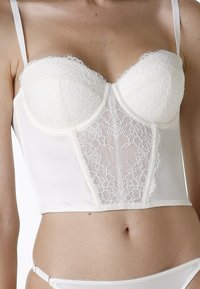 Bustier in pizzo color crema con coppe strutturate, pannello in pizzo floreale trasparente al centro, spalline regolabili, corpetto aderente, finitura in satin liscia.
